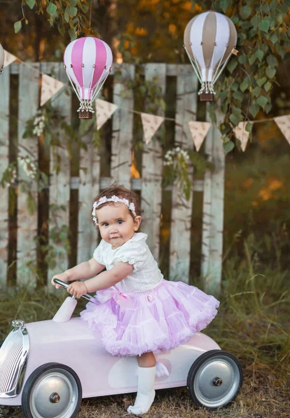 Baby with inflatable hot air balloon decorations in a garden setting, perfect for baby shower or nursery decor.