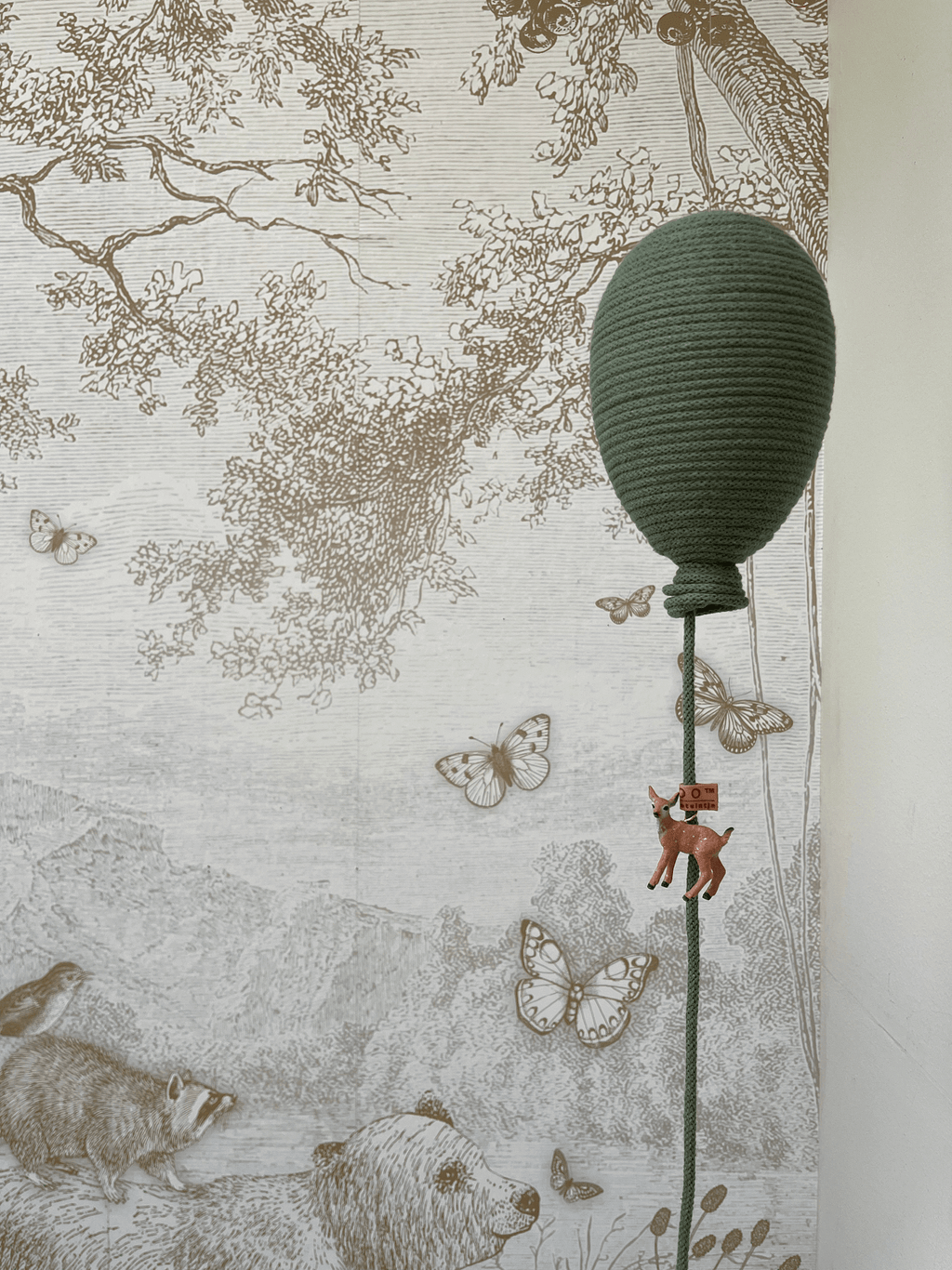 Handmade eucalyptus hot air balloon decoration with bear charm against a nature-themed wallpaper backdrop.