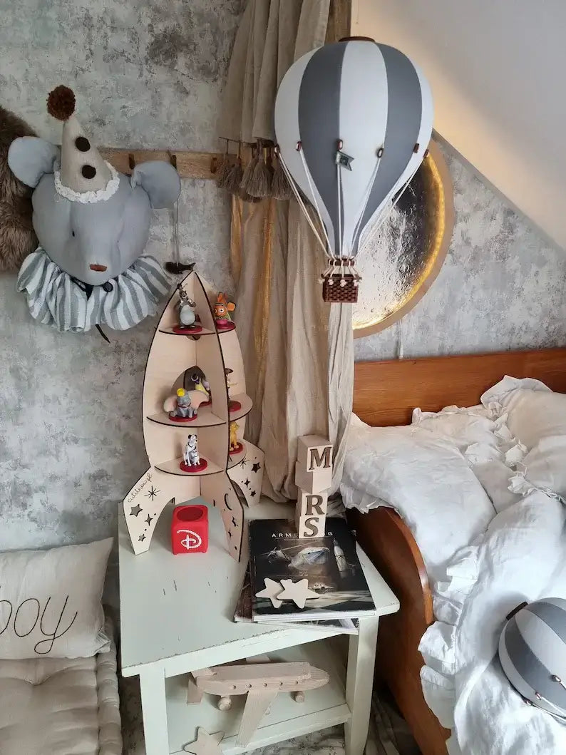 Inflatable hot air balloon decoration in a child's room with soft grey and white colors, surrounded by nursery decor and toys.