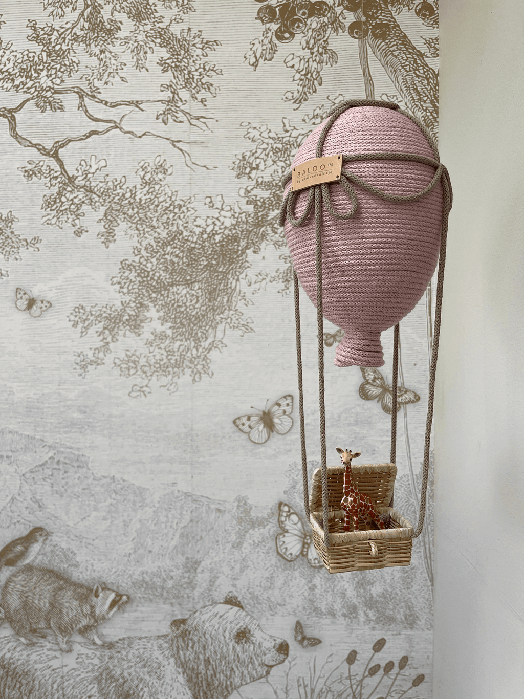 Powder pink decorative hot air balloon hanging with giraffe figurine in a nursery setting.