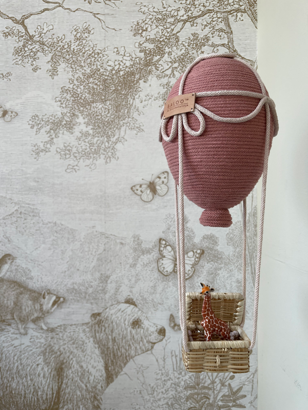 Blush Baloo hot air balloon decoration for baby nursery with giraffe in basket, handcrafted detail, against animal-themed wallpaper.