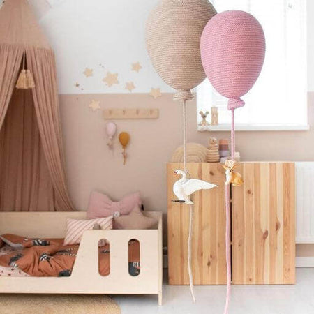 Pink and beige hot air balloon decorations hanging in a baby nursery with cozy decor and wooden furniture.