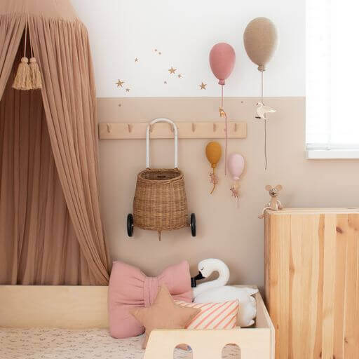 Baby nursery with powder pink hot air balloon decor, canopy, wicker basket, and plush toys, creating a cozy and whimsical atmosphere.