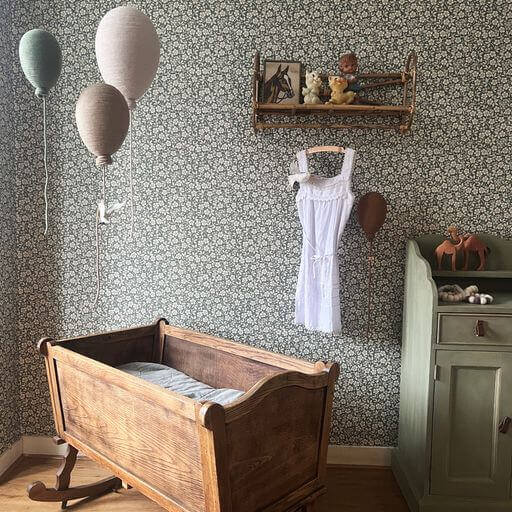 Vintage nursery with wooden cradle and Baloo inflatable hot air balloon decorations on floral wallpaper.