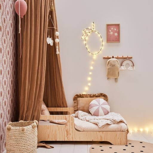 Boho-style baby nursery with wooden bed, canopy, and pink hot air balloon decor hanging from the ceiling.